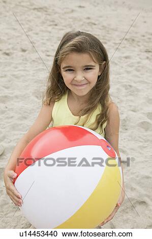 Stock Image - Portrait of girl holding beachball on beach, smiling. Fotosearch