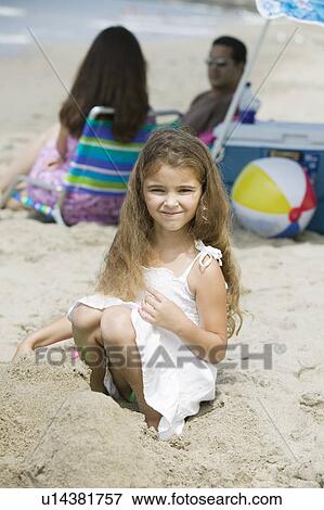 Stock Photo - Portrait of girl on beach, parents in background. Fotosearch