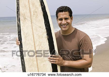 Picture - Portrait of man holding surfboard on beach. Fotosearch
