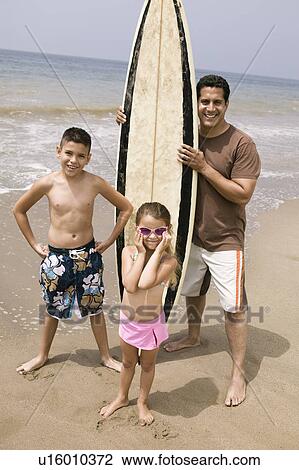 Stock Image - Portrait of man holding surfboard with children on beach . Fotosearch