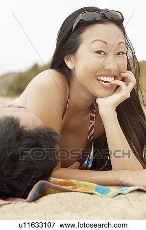 Portrait of young woman lying down on beach, nibbling finger, man's head on foreground View Large Photo Image Stock Photo - Portrait of young woman lying down on beach, nibbling finger, man's head on foreground. Fotosearch