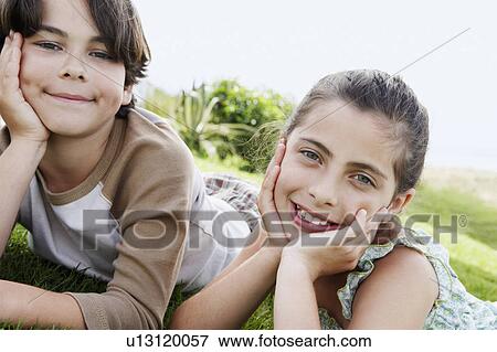 Pre-teen boy and girl reclining, hands on chin on grass View Large Photo Image Stock Photo - Pre-teen boy and girl reclining, hands on chin on grass. Fotosearch