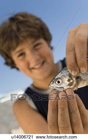 Stock Image - Pre-teen boy holding fish on beach, focus on foreground. Fotosearch