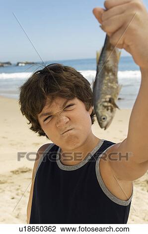 Pre-teen boy holding fish on beach, pulling face View Large Photo Image Stock Image - Pre-teen boy holding fish on beach, pulling face. Fotosearch