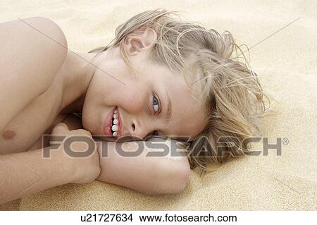 Picture - Pre-teen boy lying on arm in sand, close-up. Fotosearch