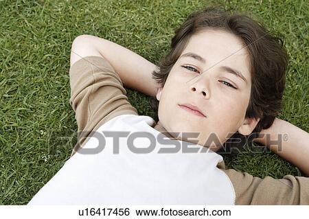 Pre-teen boy lying on back in grass, hands behind head, elevated view View Large Photo Image Stock Photograph - Pre-teen boy lying on back in grass, hands behind head, elevated view. Fotosearch