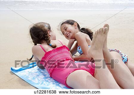 Pre-teen girls lying side by side on stomach on beach towel on sandy beach, talking View Large Photo Image Stock Photo - Pre-teen girls lying side by side on stomach on beach towel on sandy beach, talking. Fotosearch