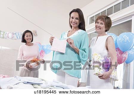 Stock Photography - Pregnant woman displaying new gift at baby shower. Fotosearch