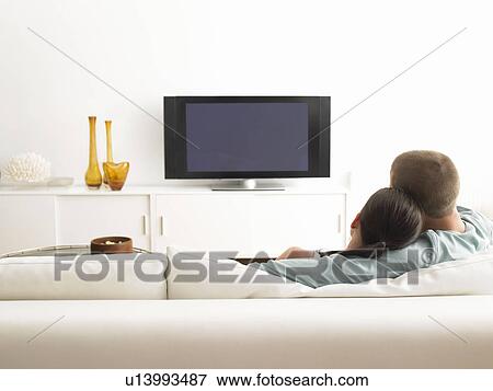 Stock Photo - Rear View of couple on sofa watching TV. Fotosearch
