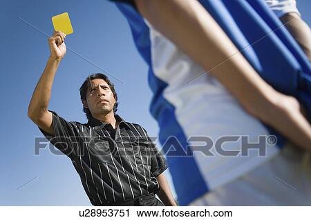 Stock Image - Referee holding up yellow card, portrait, low angle view. Fotosearch