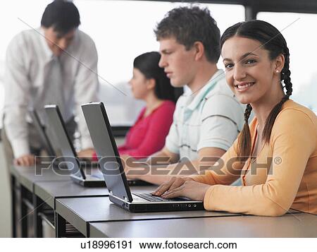Stock Image - Row of teenage students using laptops in classroom. Fotosearch