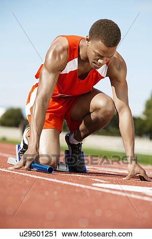 Stock Image - Runner Waiting in Starting Block holding Baton. Fotosearch