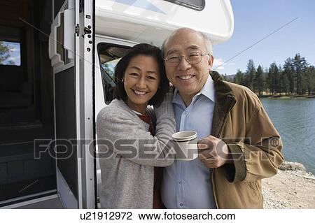 Stock Image - Senior couple embracing outside of RV on lake. Fotosearch