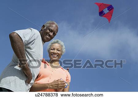 Stock Photo - Senior couple flying kite, outdoors, (low angle view), (portrait). Fotosearch