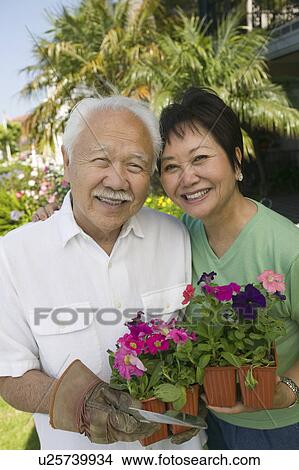Picture - Senior couple holding flowers, outdoors, (portrait). Fotosearch