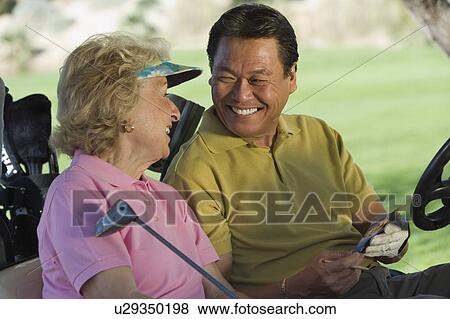 Stock Photo - Senior couple in golf cart, smiling. Fotosearch