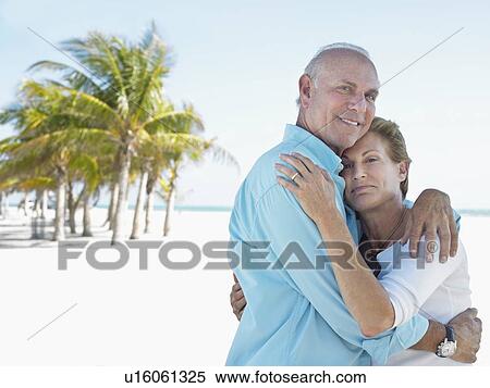 Stock Photography - Senior couple on beach embracing on tropical beach. Fotosearch