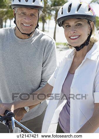 Stock Image - Senior couple on bicycles on tropical beach, close up. Fotosearch