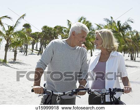 Stock Photo - Senior couple on bicycles on tropical beach. Fotosearch