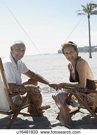 Stock Image - Senior couple on sunloungers on tropical beach. Fotosearch
