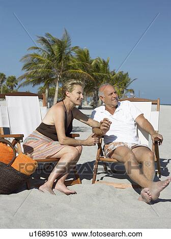 Stock Image - Senior couple on sunloungers on tropical beach. Fotosearch