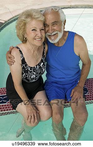 Stock Photo - Senior Couple sitting on edge of swimming pool, elevated view portrait.. Fotosearch