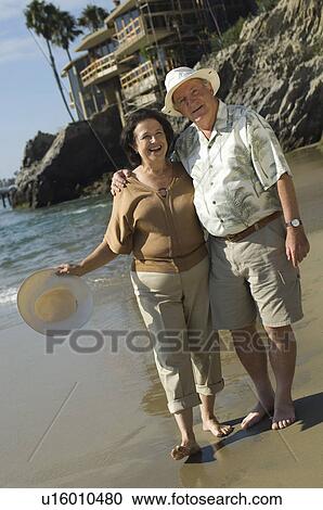 Stock Image - Senior couple walking on beach. Fotosearch