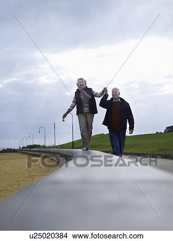 Senior couple walking on wall, holding hands View Large Photo Image Picture - Senior couple walking on wall, holding hands. Fotosearch