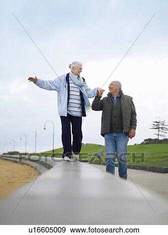 Stock Photo - Senior couple walking on wall, holding hands. Fotosearch