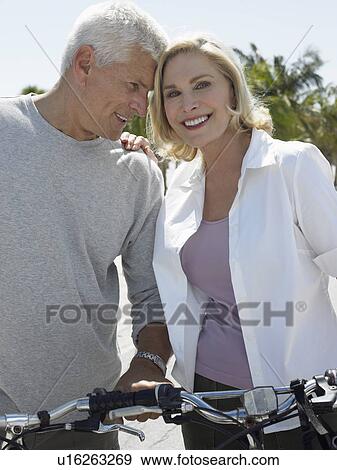 Stock Photo - Senior couple with bicycles on tropical beach. Fotosearch