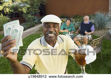 Stock Image - Senior golfers celebrating success, focus on man showing banknotes, (portrait). Fotosearch