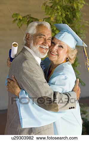 Stock Image - Senior graduate hugging husband outside. Fotosearch