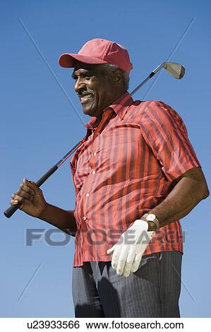 Stock Photograph - Senior man holding golf club, (low angle view). Fotosearch