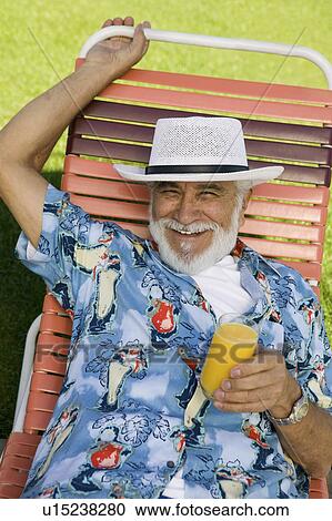 Stock Image - Senior Man lying on lawn chair Holding Orange Juice, elevated view portrait.. Fotosearch