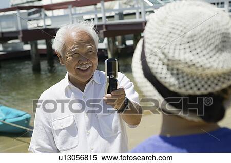Senior man photographing wife using camera phone, outdoors View Large Photo Image Stock Photography - Senior man photographing wife using camera phone, outdoors. Fotosearch