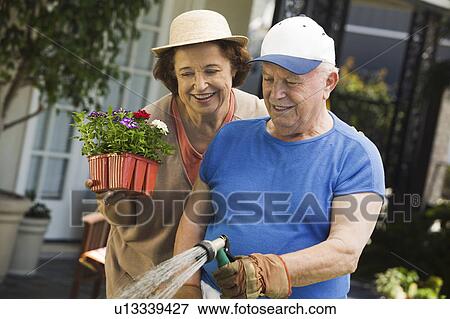 Senior woman assisting husband watering plants in garden View Large Photo Image Stock Photo - Senior woman assisting husband watering plants in garden. Fotosearch
