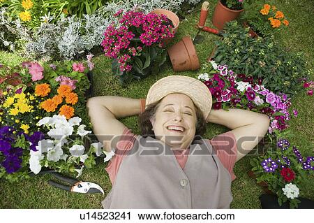 Stock Image - Senior woman lying on ground among flowers, smiling, (overhead view). Fotosearch