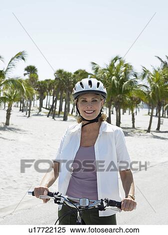 Stock Photography - Senior woman on bicycle on tropical beach. Fotosearch