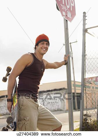 Stock Photo - Skateboarder leaning on stop sign in street, portrait. Fotosearch