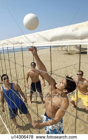Stock Photo - Small group of young men playing volleyball on beach. Fotosearch