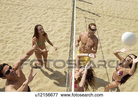 Stock Photo - Small group of young people playing volleyball on sandy beach, elevated view. Fotosearch
