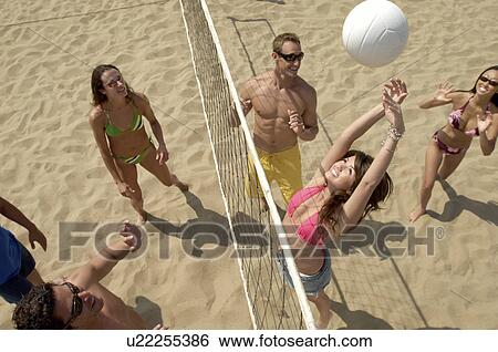 Stock Photograph - Small group of young people playing volleyball on sandy beach, elevated view. Fotosearch