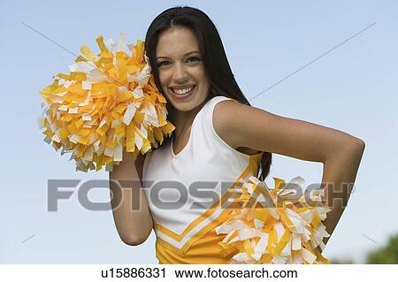 Stock Image - Smiling Cheerleader holding pom-poms, (portrait). Fotosearch