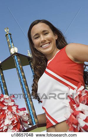 Stock Photo - Smiling Cheerleader holding trophy, (portrait), (low angle view). Fotosearch