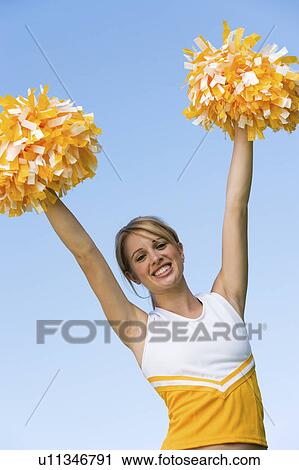 Stock Image - Smiling Cheerleader rising pom-poms, (portrait), (low angle view). Fotosearch