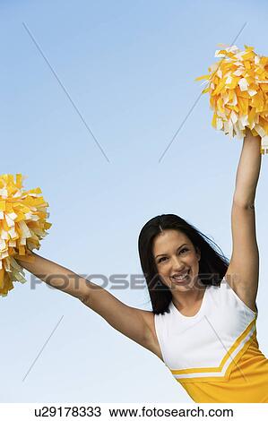 Stock Image - Smiling Cheerleader rising pom-poms, (portrait). Fotosearch