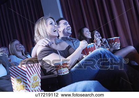 Smiling Couple sitting, arms around, Watching Movie in theatre View Large Photo Image Stock Image - Smiling Couple sitting, arms around, Watching Movie in theatre. Fotosearch