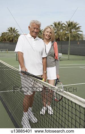 Smiling Couple standing on Tennis Court near net, holding rackets View Large Photo Image Stock Image - Smiling Couple standing on Tennis Court near net, holding rackets. Fotosearch