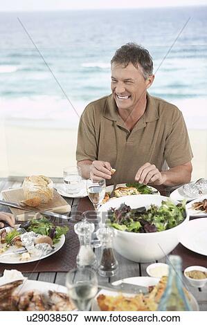Smiling Man Eating meal outside near the sea View Large Photo Image Stock Photo - Smiling Man Eating meal outside near the sea. Fotosearch