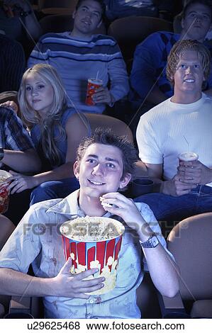 Stock Photo - Smiling Man Eating Popcorn, watching movie in Theatre. Fotosearch